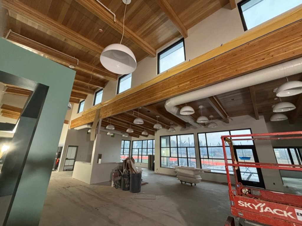 Open lobby with glulam beams and rows of pendant lights during construction of the Vancouver, WA DSHS clinic