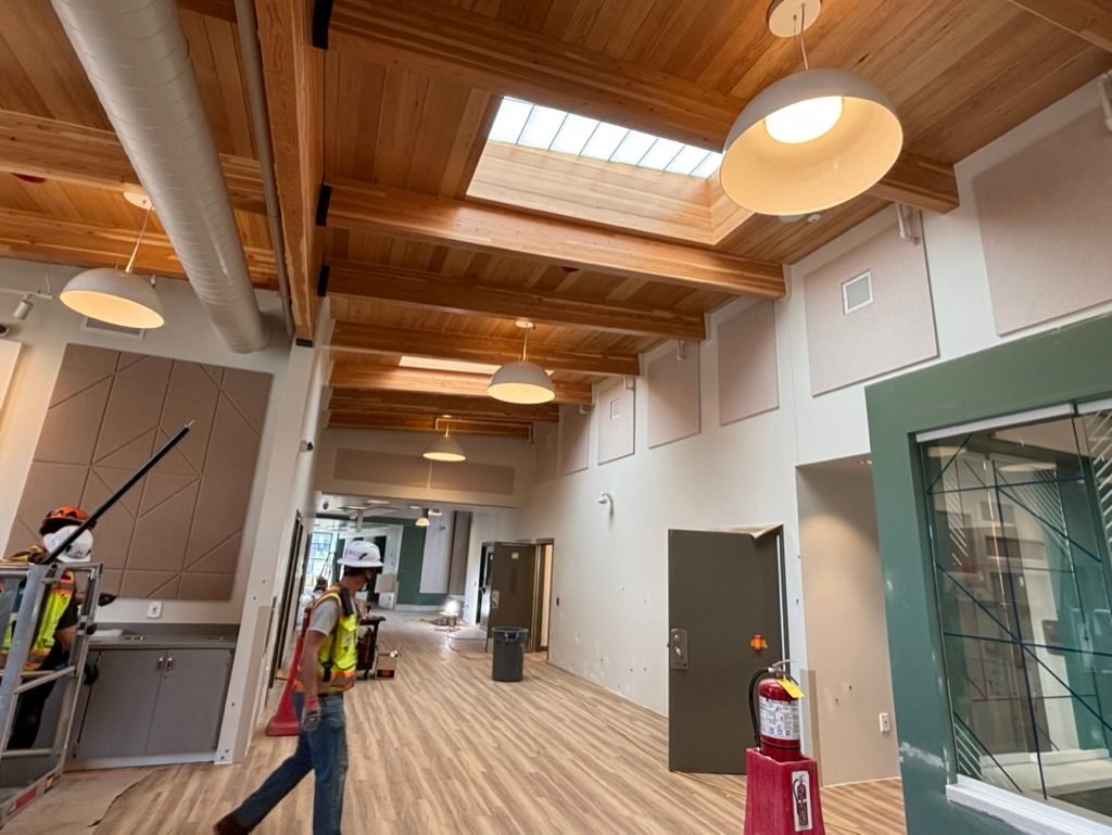 Electricians working in a skylit corridor with exposed timber beams during the DSHS clinic build in Vancouver, WA