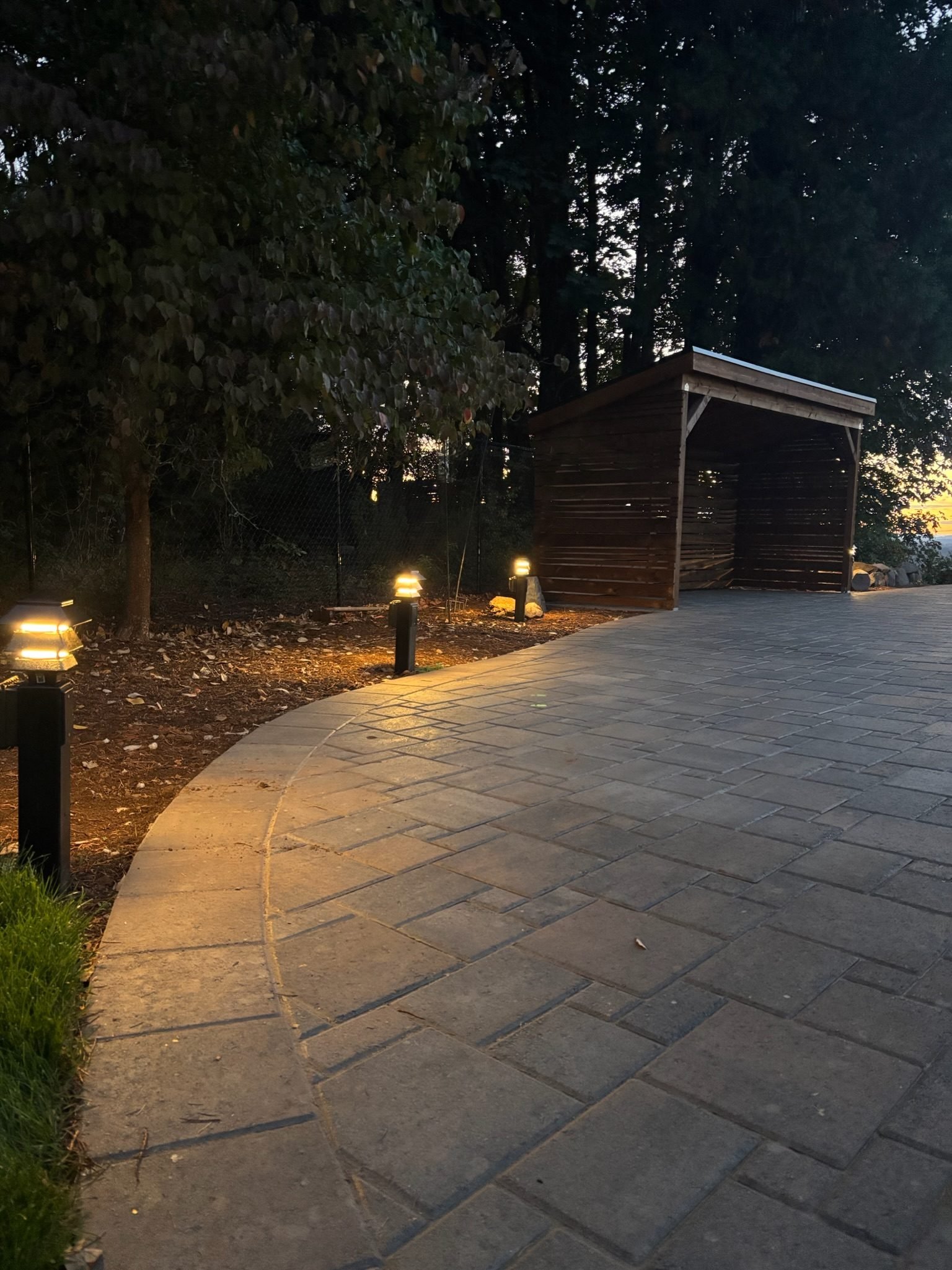 Landscape path lights glowing beside a paver patio and wood shelter at sunset in Oregon City, OR