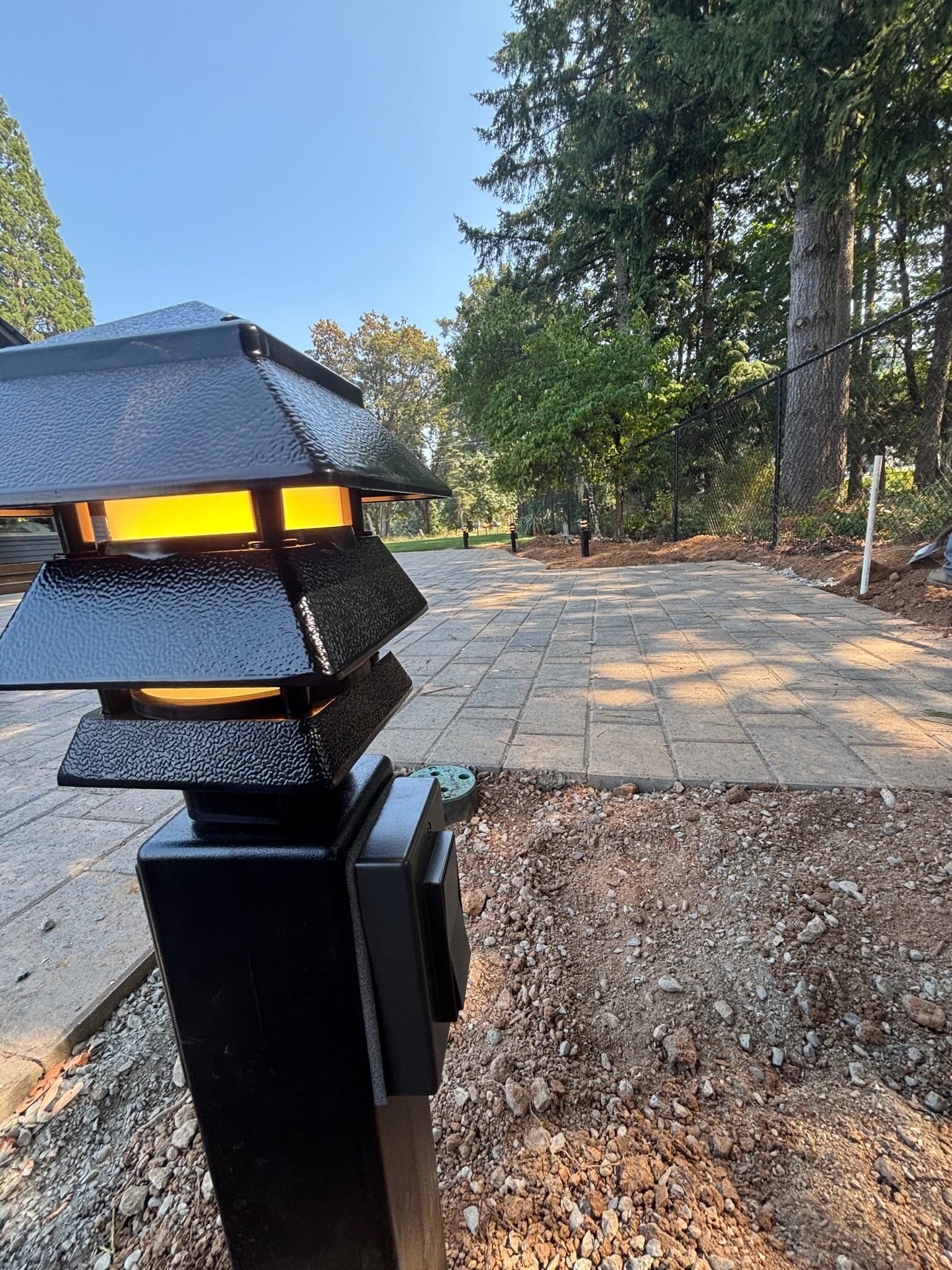 Close-up of a black pagoda path light on a post with a built-in outdoor receptacle beside a paver patio in Oregon City, OR